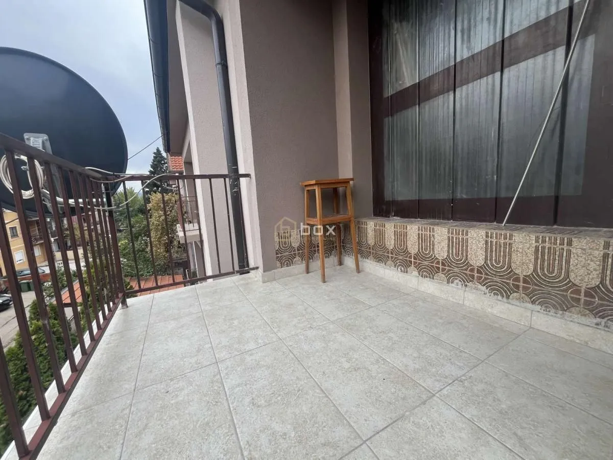 Small tiled balcony with a metal railing and a wooden stool.