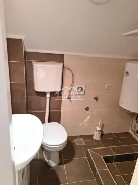 Smaller bathroom with brown tiles, toilet, washbasin, and water heater. - image 8