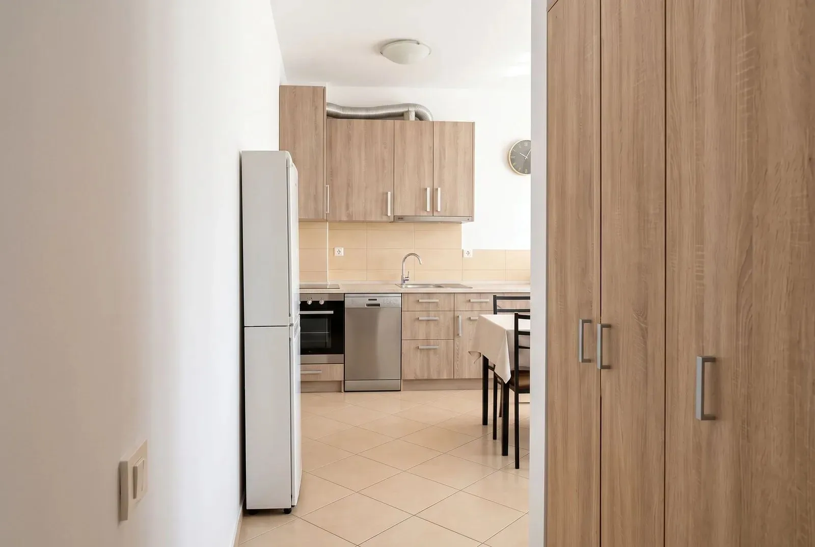 View from the hallway into the kitchen with wooden cabinets and a dining table.