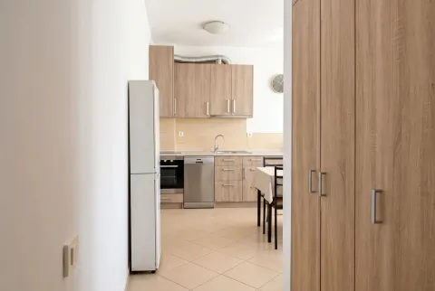 View from the hallway into the kitchen with wooden cabinets and a dining table. - image 3