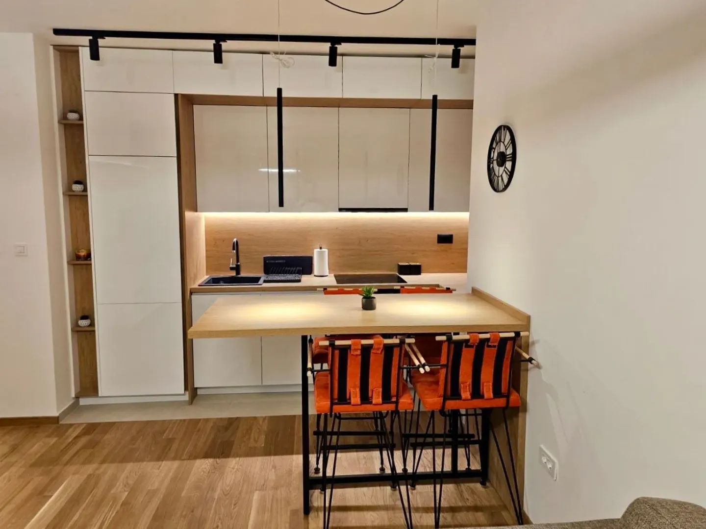 Moderna kuhinja sa bijelim elementima, drvenim detaljima i šankom za ručavanje.