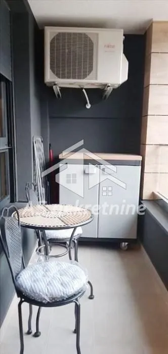 Manji namešteni balkonski prostor sa stolom, stolicama i klima uređajem.