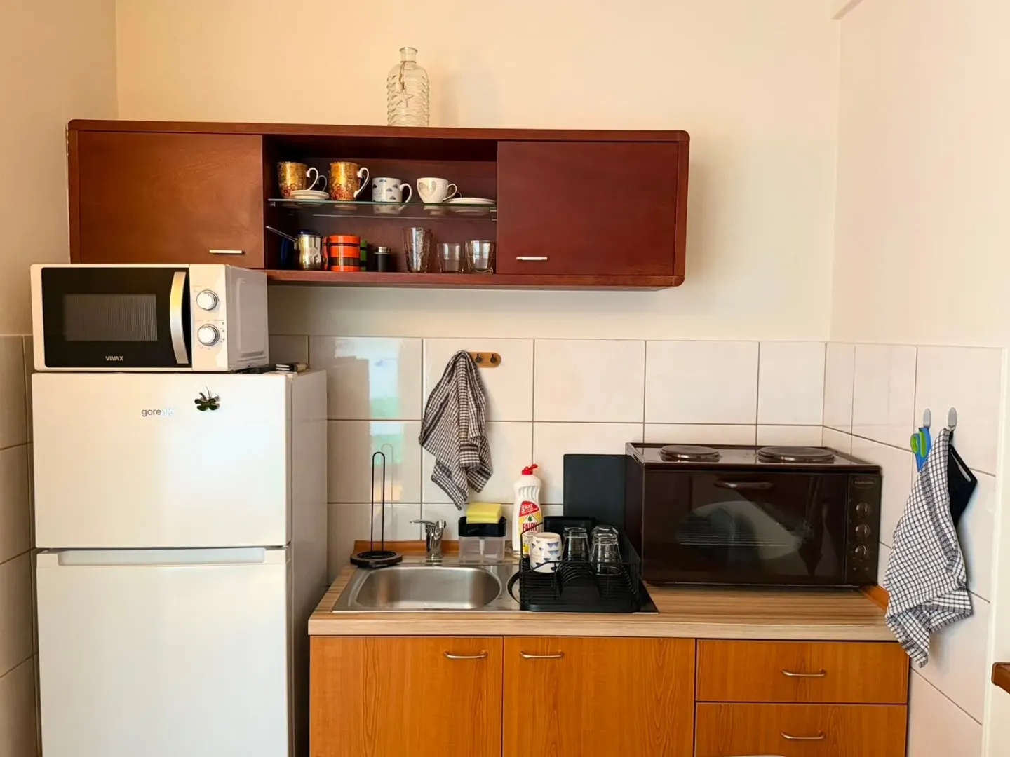 Manja kuhinja sa sudoperom, frižiderom i kuhinjskim elementima.