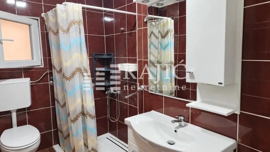 Small bathroom with a shower cabin, washbasin, and toilet, tiled in dark tiles.