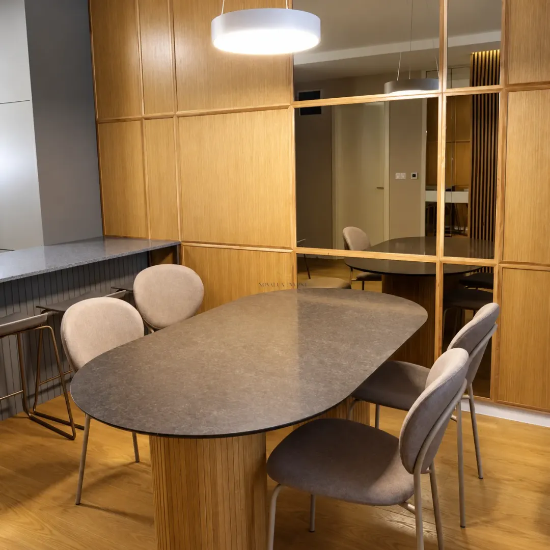 Dining area with a modern oval table and upholstered chairs against a wooden wall panel.