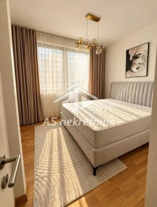 Furnished bedroom with a double bed, large window, and modern chandelier.