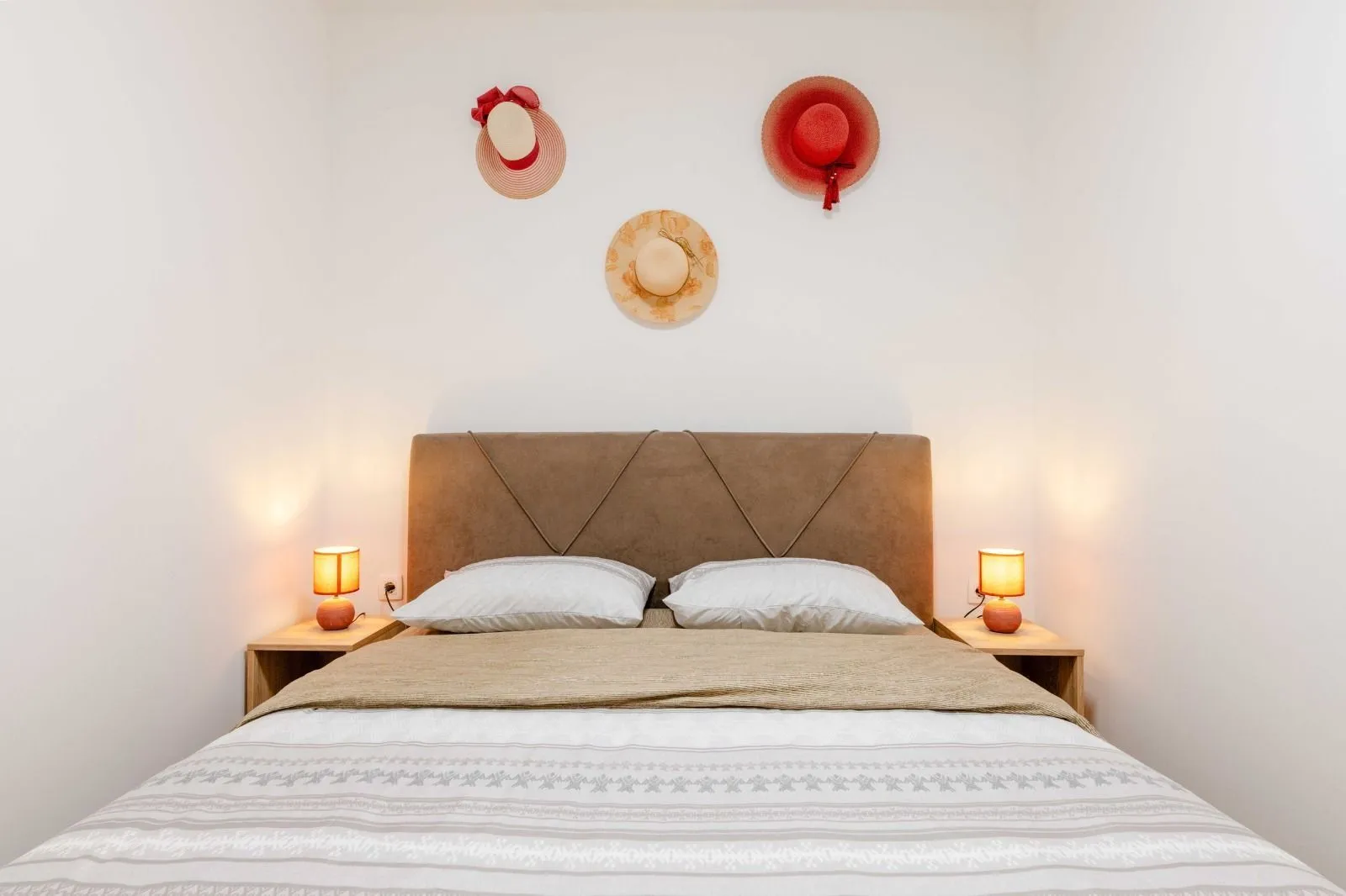 Bedroom with a double bed, bedside tables, and decorative hats on the wall.
