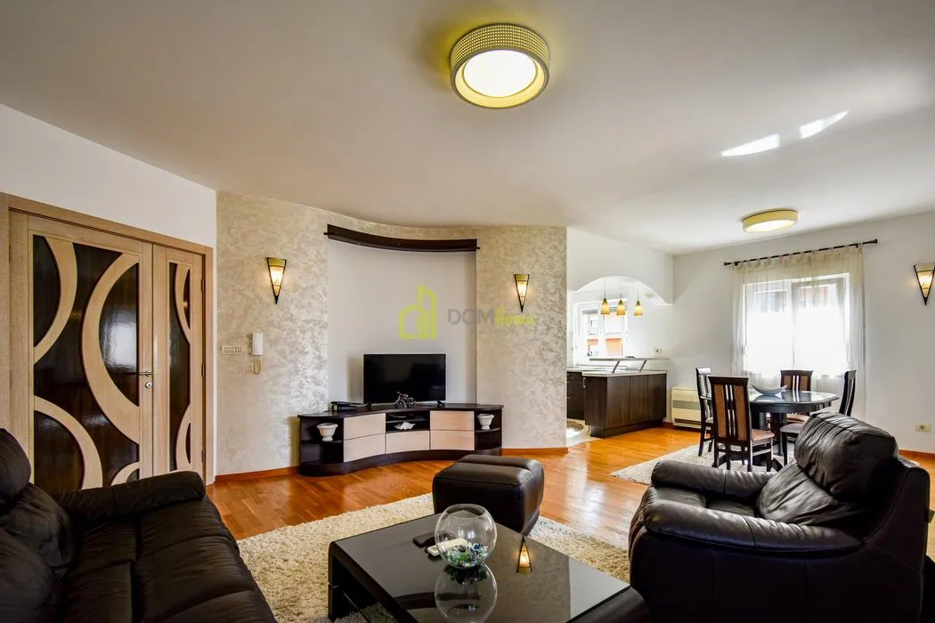 Spacious living room with sofa set, TV, and dining area in the background.