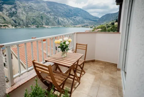 Balkon sa drvenim stolom, stolicama i vazom sa cvijećem, sa pogledom na more i planine. - image 12