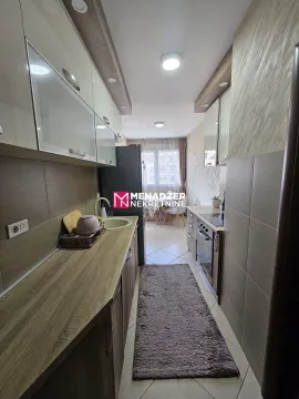 Narrow kitchen with wood-patterned elements and a dining area in the background. - image 3