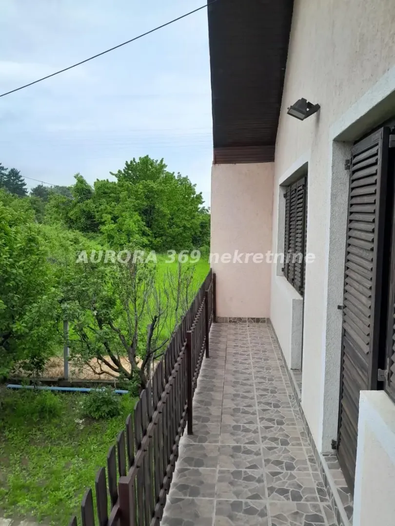 Natkriveni balkon sa popločanim podom i pogledom na zelenilo i dvorište.