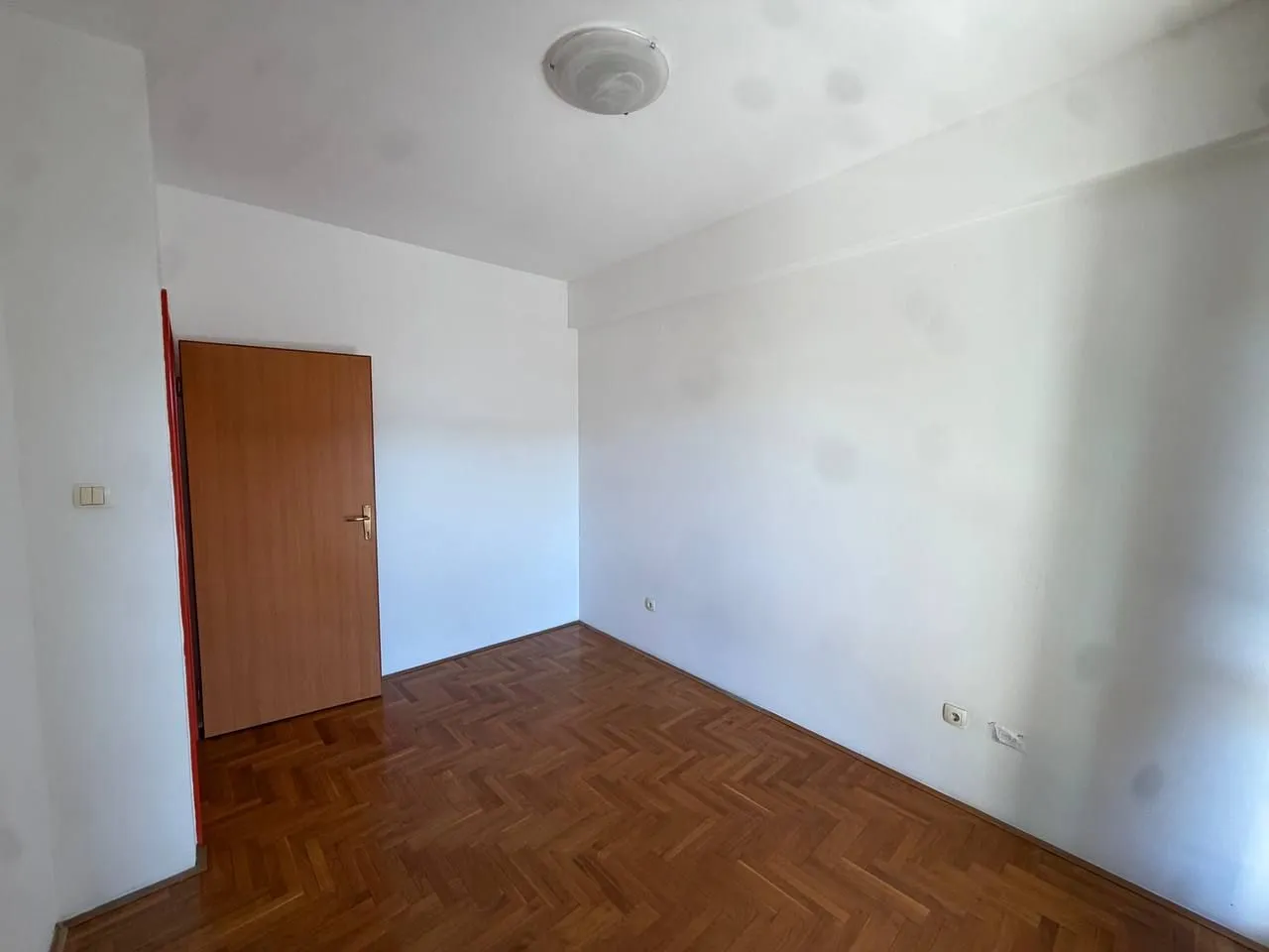 Empty room with parquet flooring and a wooden door.