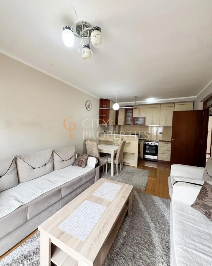 Living room with a sofa, coffee table, and a view of the dining area and kitchen in the background.