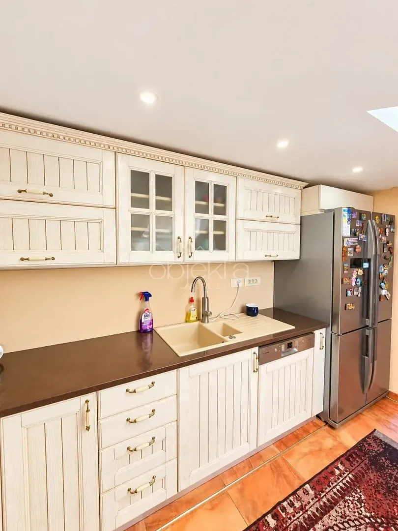 Kitchen with light wooden cabinetry, dark countertops, and a refrigerator.