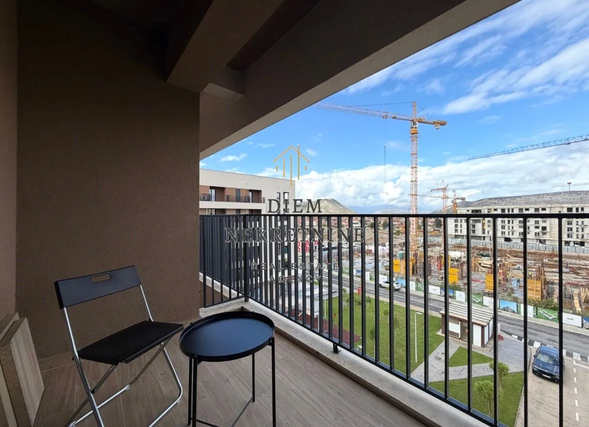Covered balcony with a chair, a small table, and a view of a construction site.