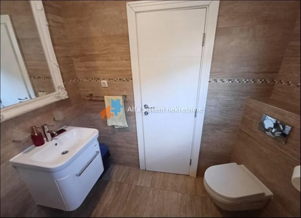 Kupatilo obloženo keramičkim pločicama sa umivaonikom i WC šoljom.