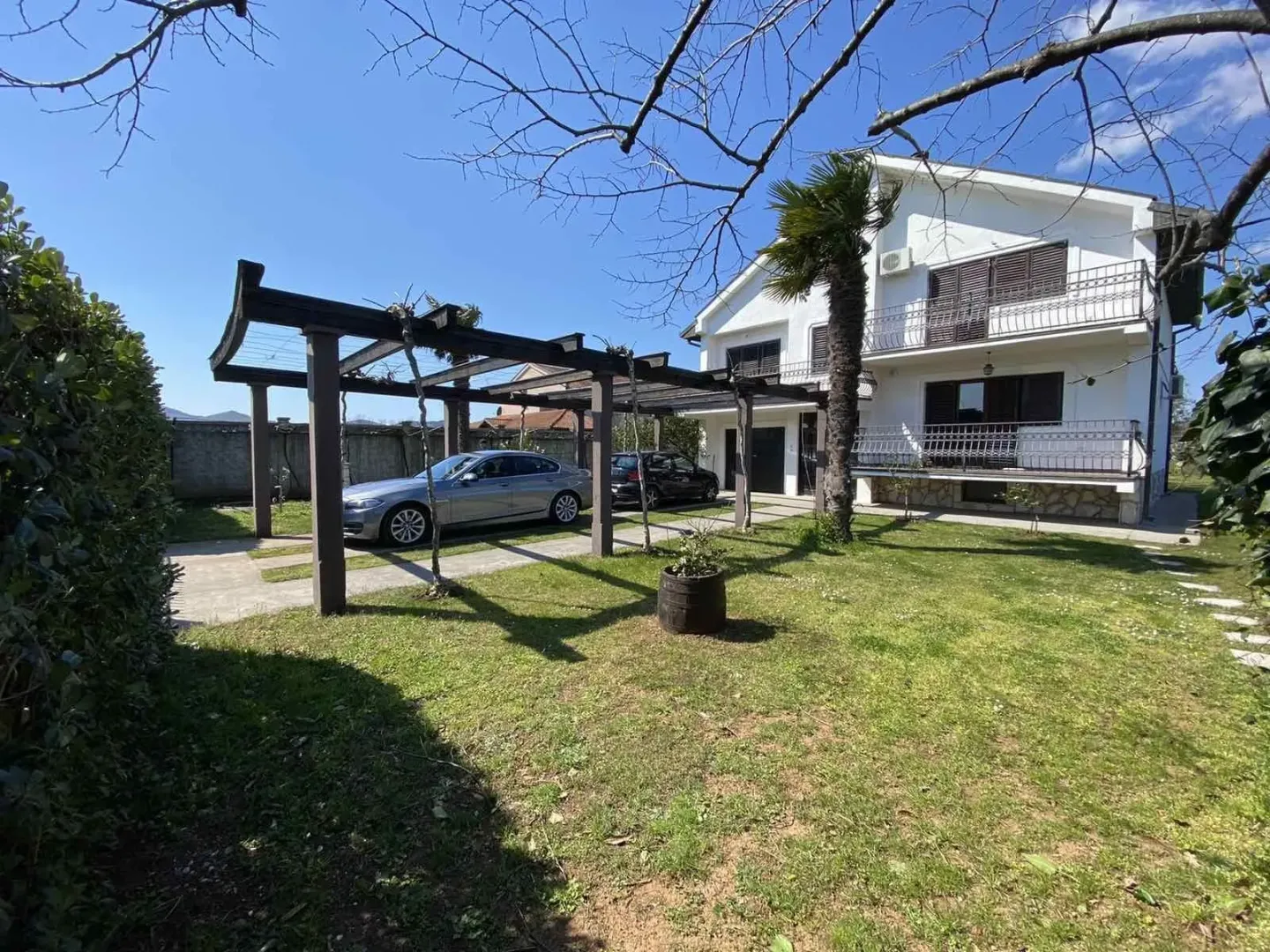 Two-story house with a landscaped yard, parking space, and wooden pergola.