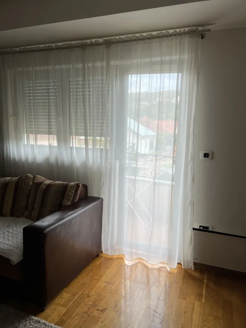 Living room with a leather sofa next to balcony doors with white curtains.
