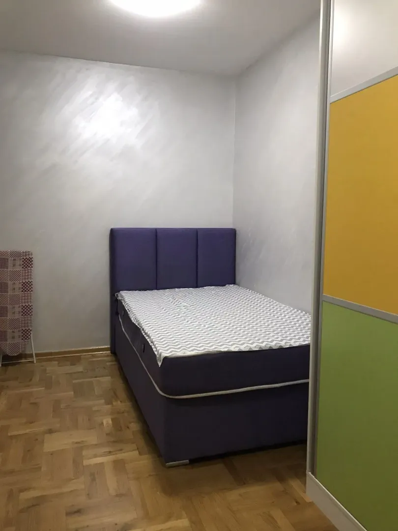 A simple bedroom featuring a purple bed and parquet flooring.