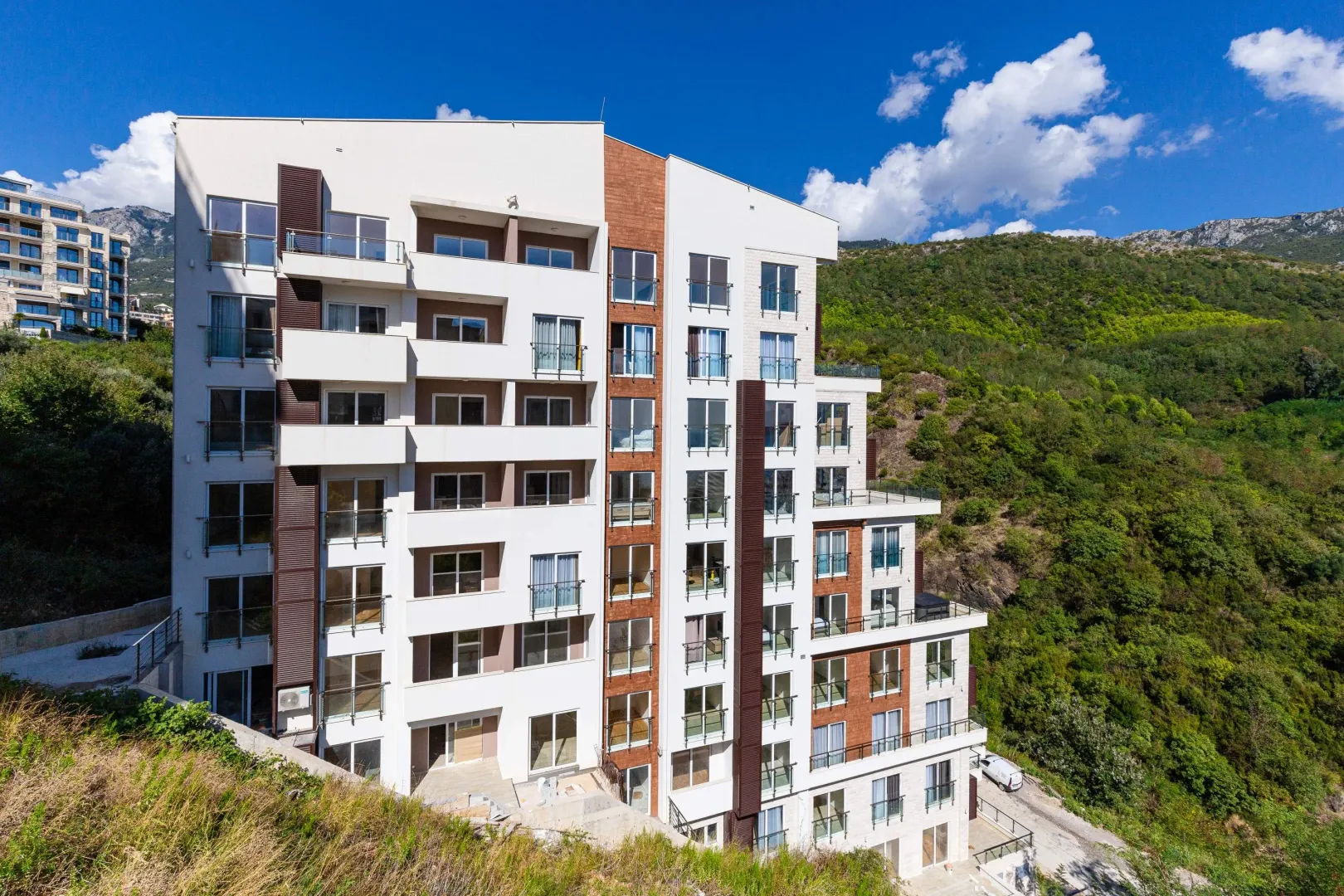 Pogled na spoljašnjost moderne stambene zgrade sa terasam i okruženjem.