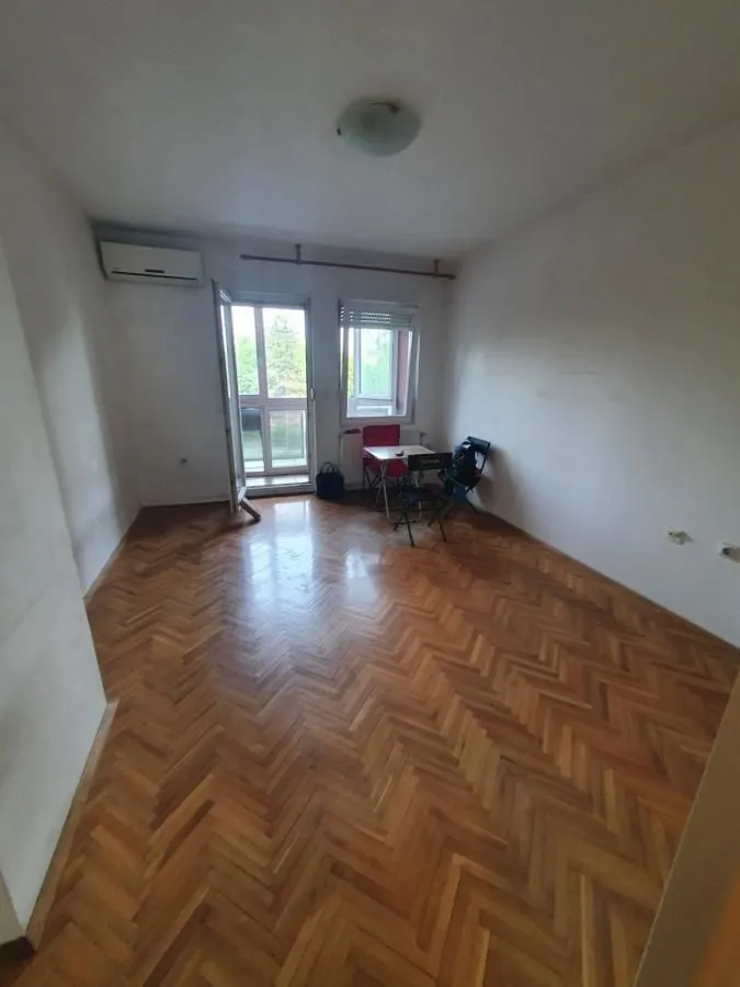 Prazna prostorija sa parketom i izlazom na balkon.