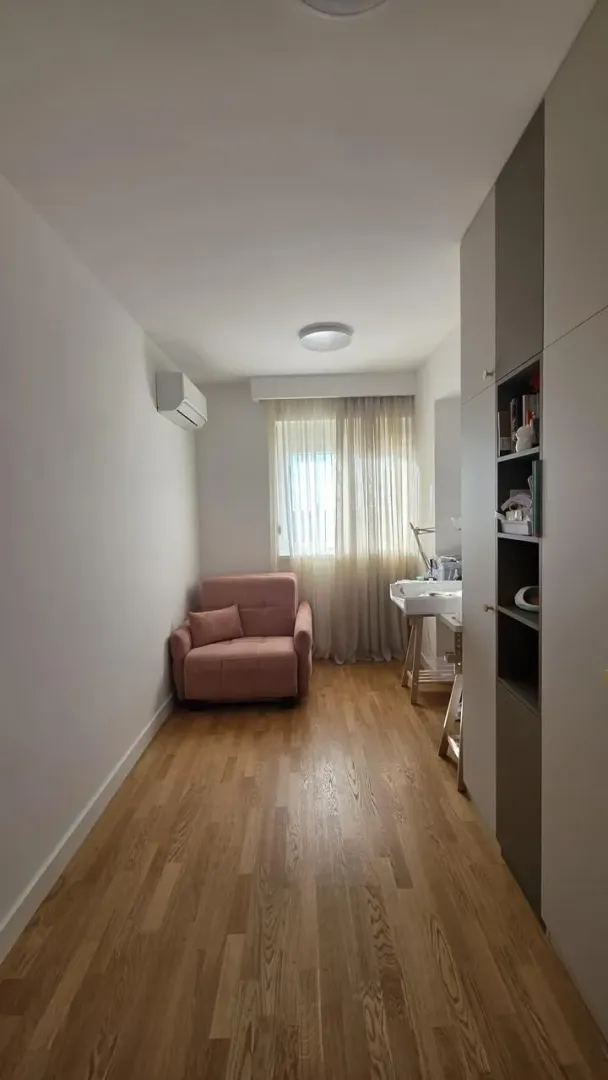 Manja spavaća soba sa roze foteljom, ugradnim plakarom i drvenim podom.