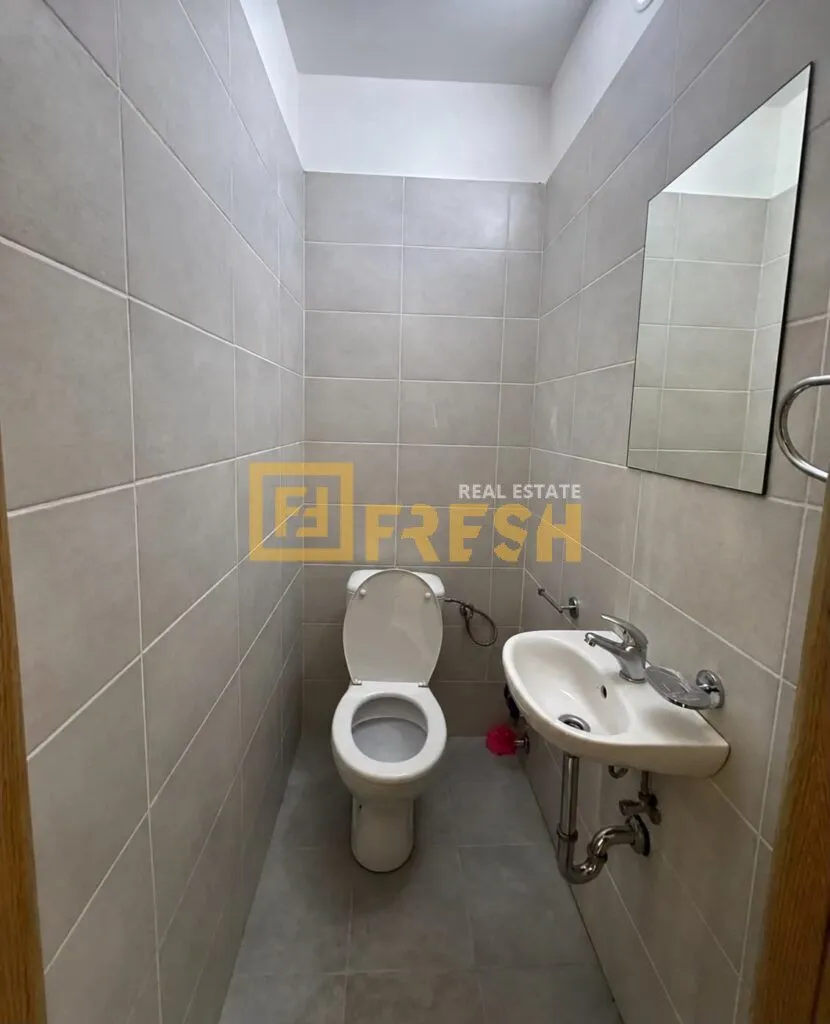 Small bathroom tiled in grey with a toilet, washbasin, and mirror.