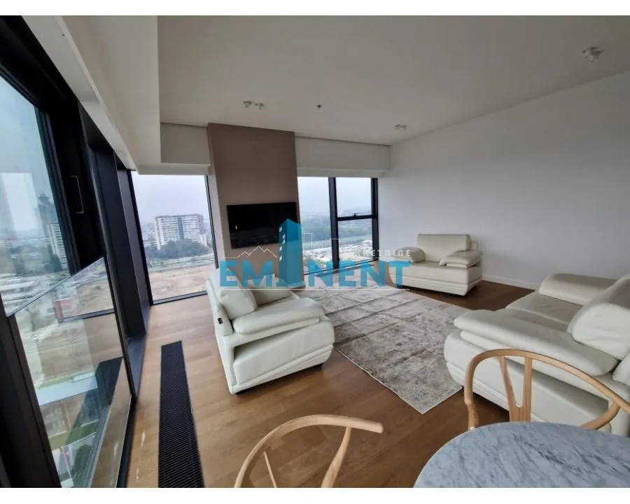 Spacious living room with seating furniture and large windows with a city view.