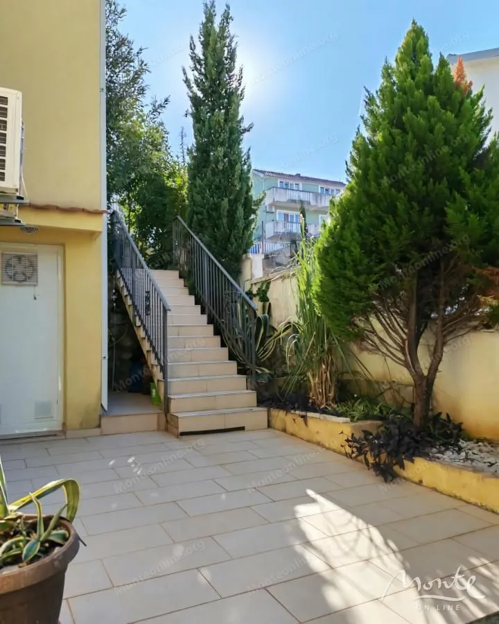 Popločano dvorište sa stepeništem i zelenilom pored kuće.
