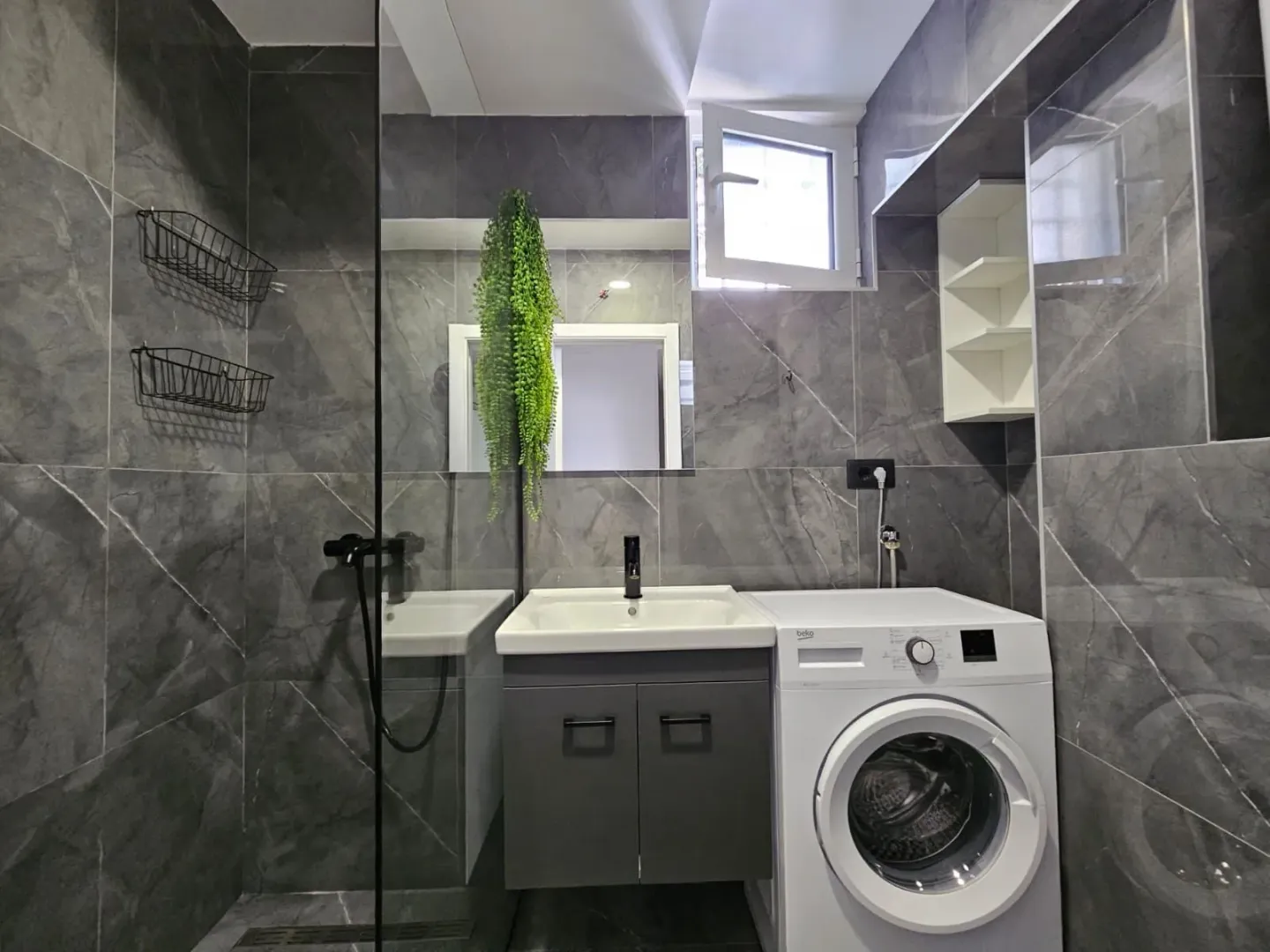 Moderne kupatilo sa tuš kabinom, umivaonikom i mašinom za veš.