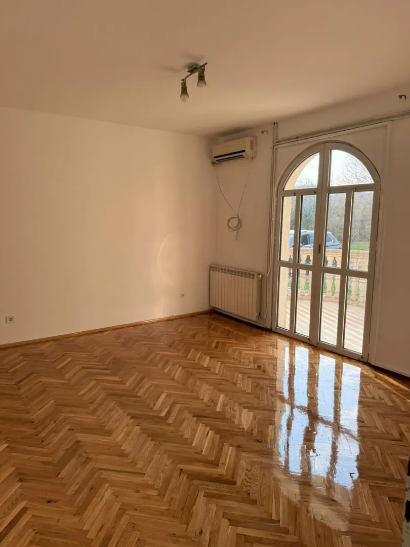 An empty room with polished parquet flooring and a large balcony door.