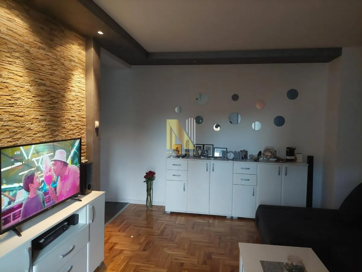 Dnevna soba sa televizorom, komodom i dekorativnim zidom od kamena.
