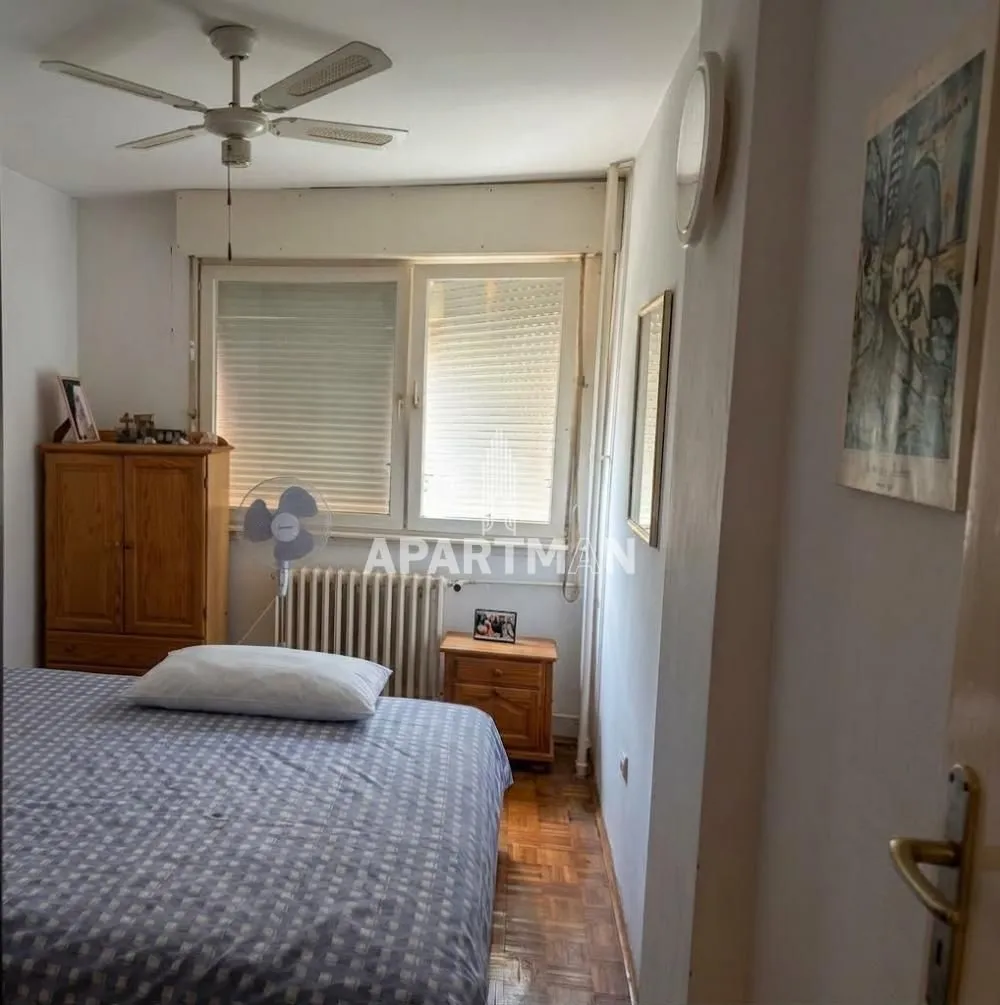 Spavaća soba sa krevetom, drvenim ormarom i plafonskim ventilatorom.