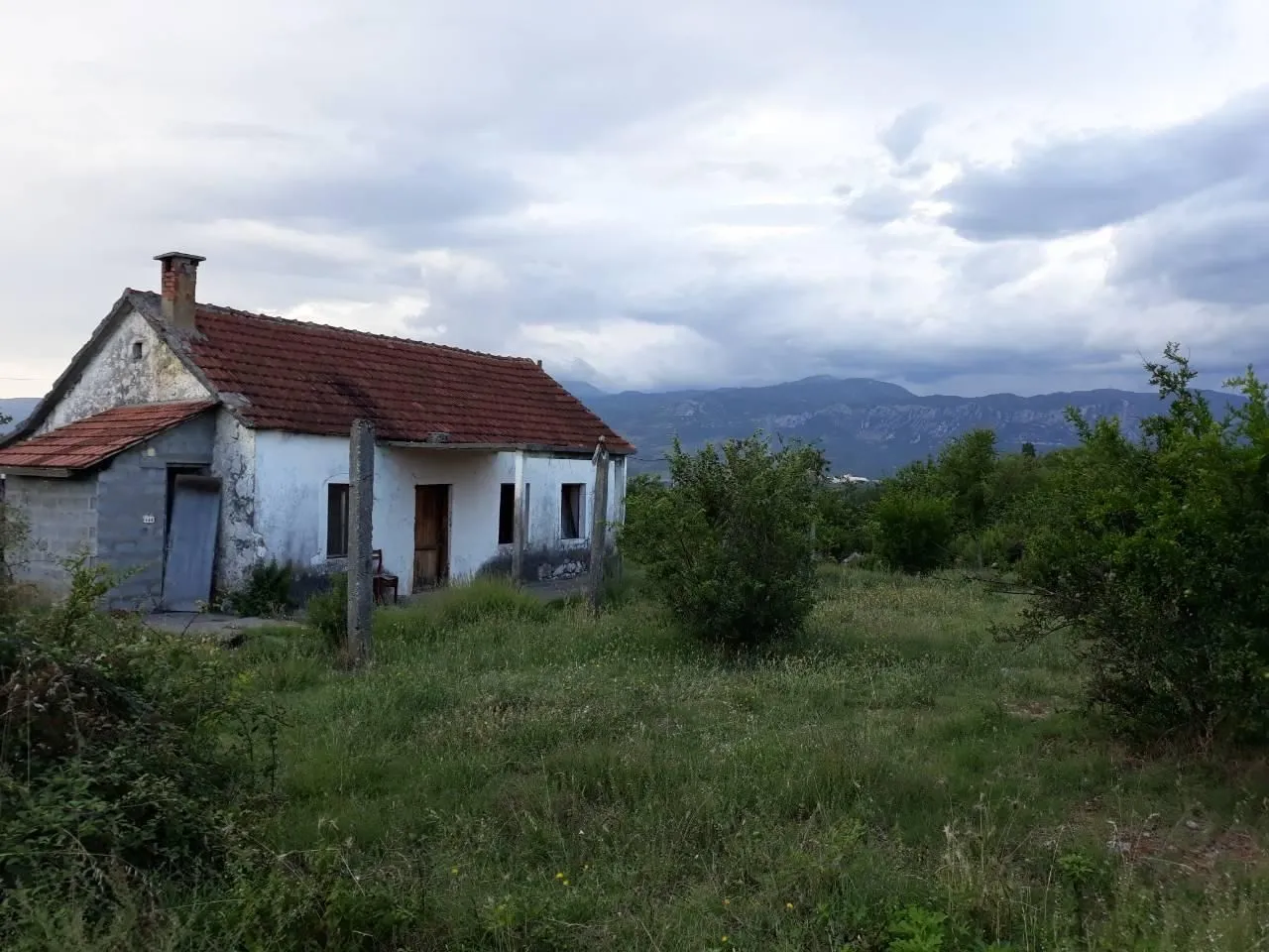 Stara prizemna kuća na prostranom placu sa pogledom na planine.