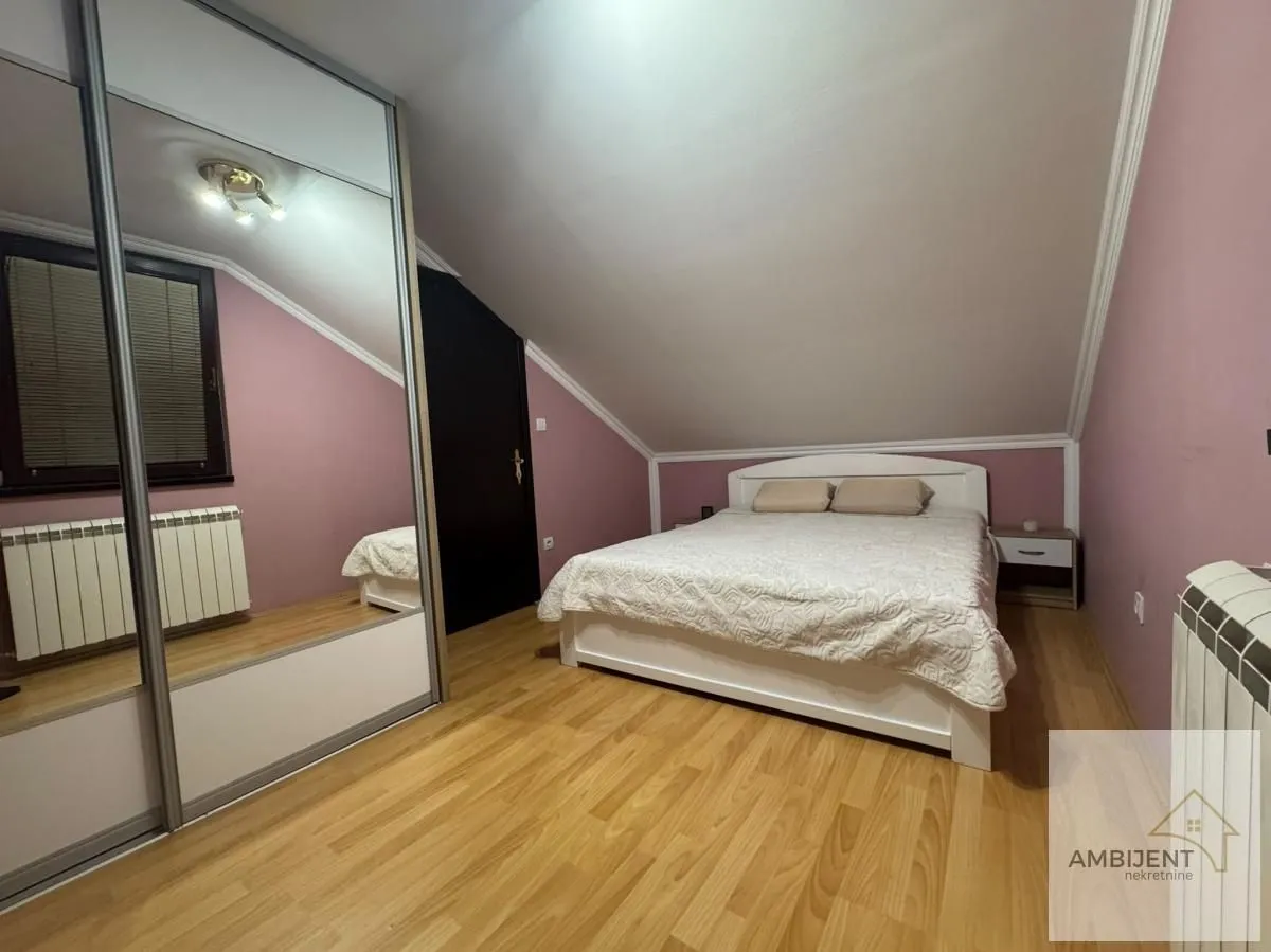 Spavaća soba sa bračnim krevetom, ormarom sa ogledalom i kosim plafonom.