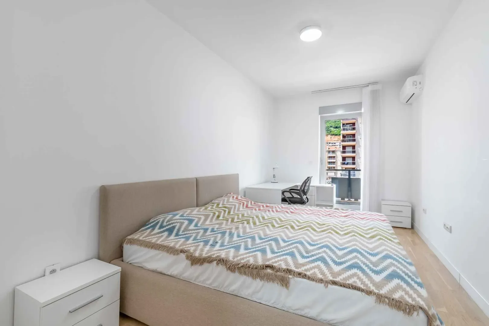 Bright bedroom with a double bed, desk, and balcony access.
