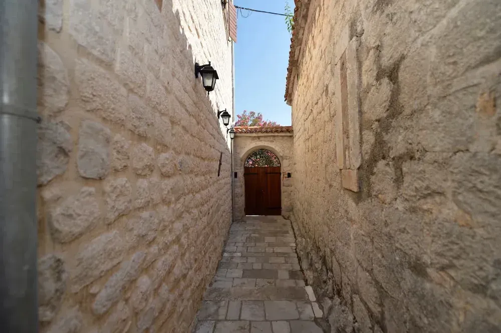 A narrow alleyway between stone walls with a paved floor and a wooden gate at the end.