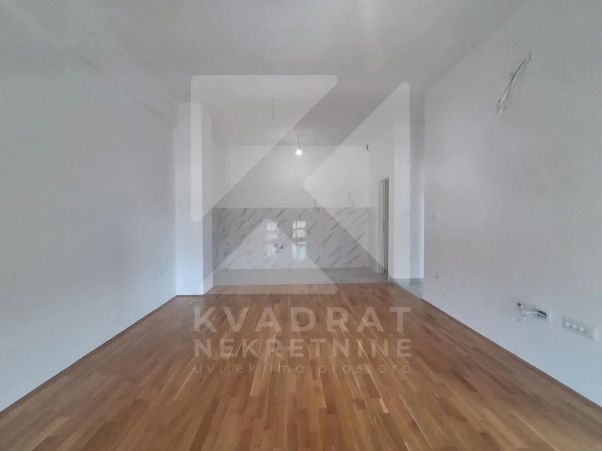 An empty room with wooden flooring and a designated kitchen area.