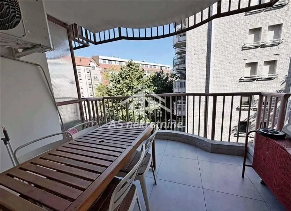 Covered balcony with a table and chairs and a view of city buildings.