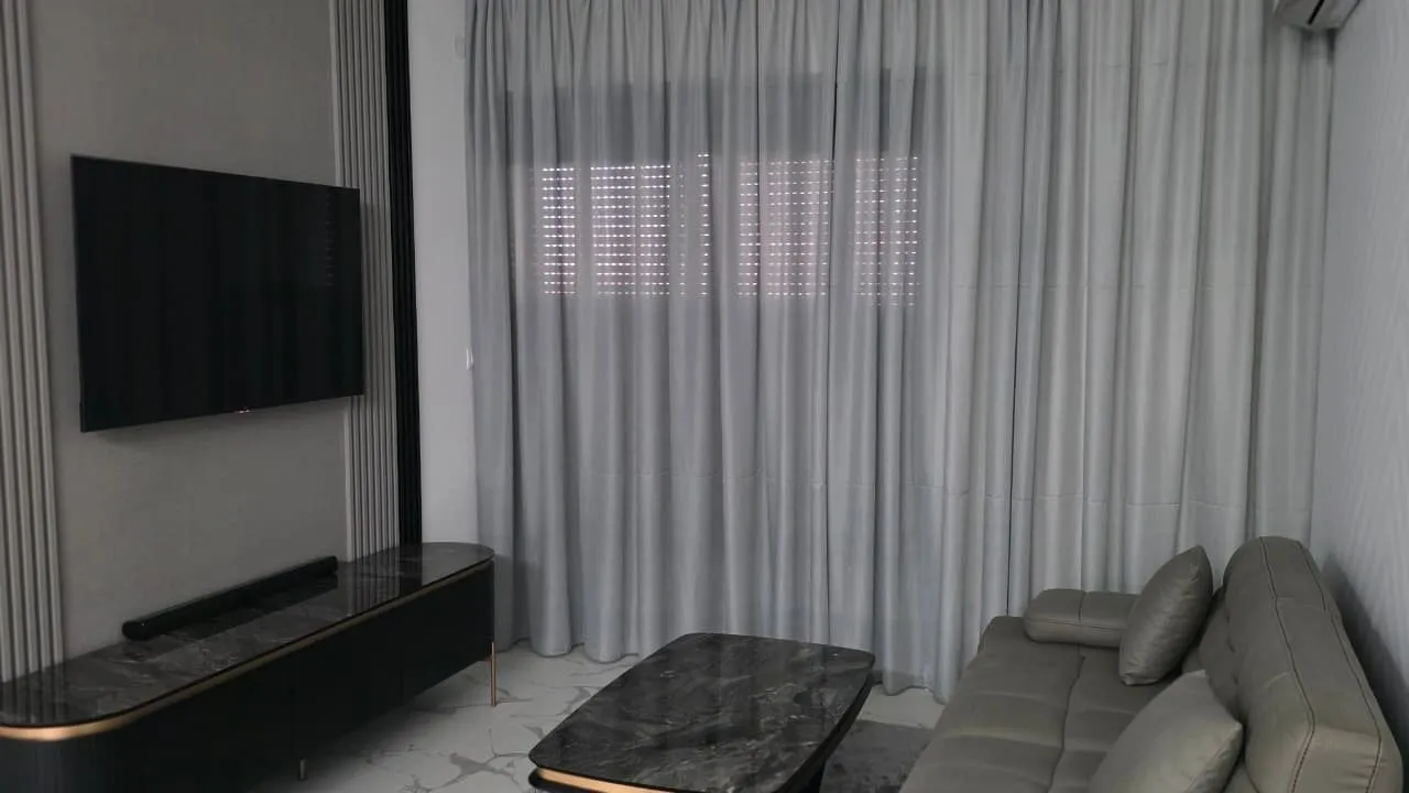 Moderna dnevna soba sa garniturom, TV-om i zavesama.