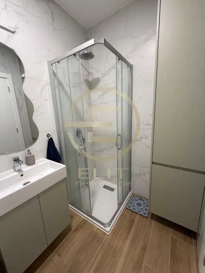 Moderno kupatilo sa tuš kabinom, umivaonikom i ogledalom.