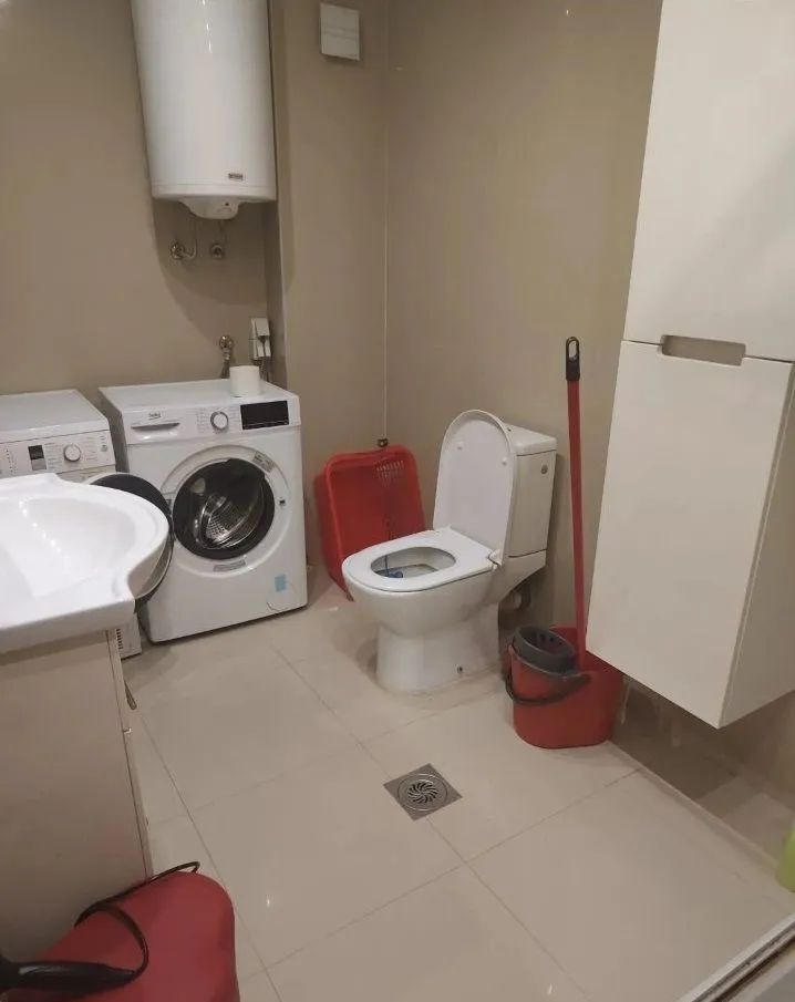 Manje uredno kupatilo sa veš mašinom, WC šoljom i bojlerom.