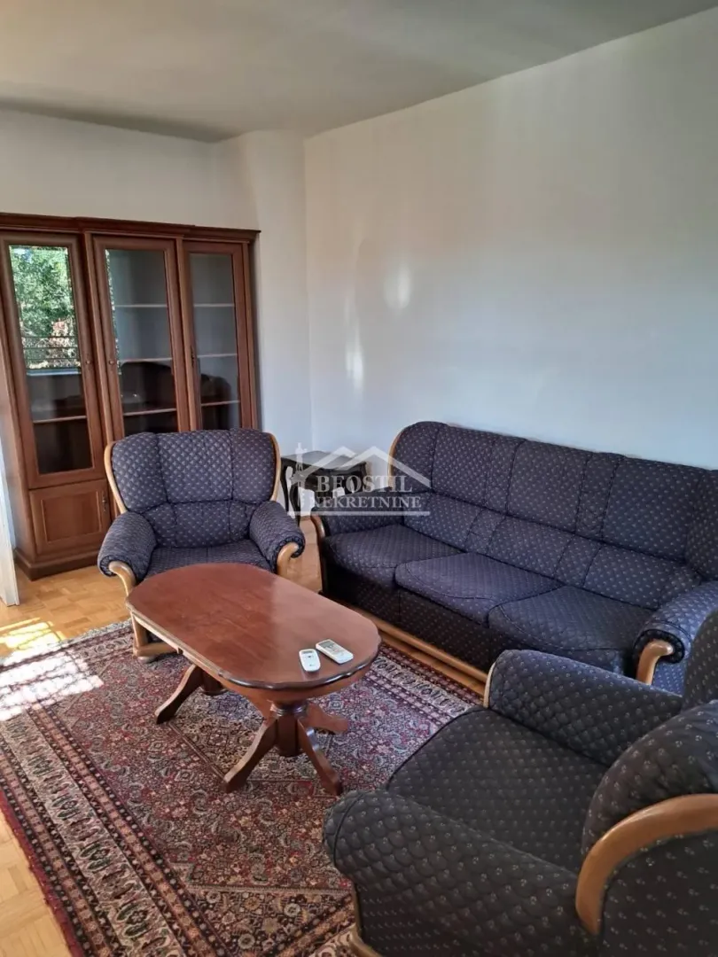 Dnevna soba sa garniturom za sedenje, drvenim stolom i vitrinom.