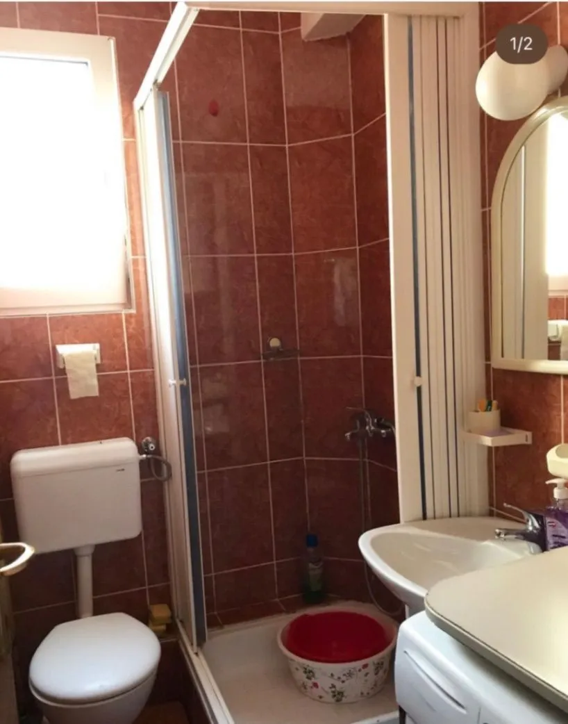 Small bathroom lined with brown tiles featuring a shower cabin, sink, and toilet.