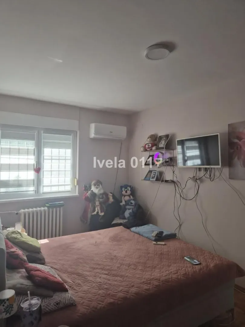 Nameštena spavaća soba sa bračnim krevetom, klima uređajem i zidnim televizorom.