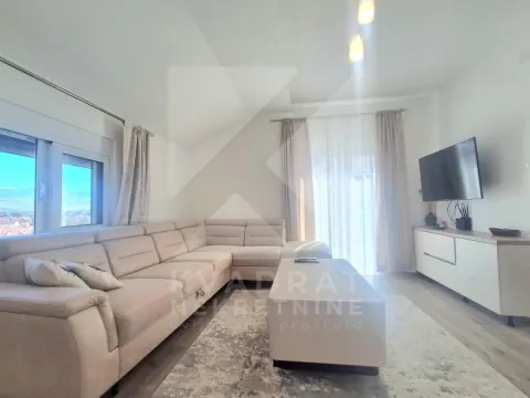 Svetao dnevni boravak sa ugaonom garniturom, stočićem i televizorom na zidu. - image 4