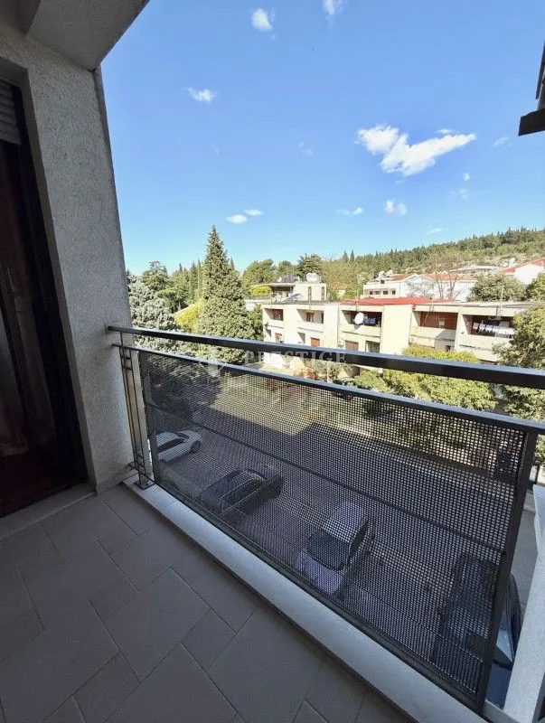 Pogled sa popločane terase na okolne zgrade i zelenilo.