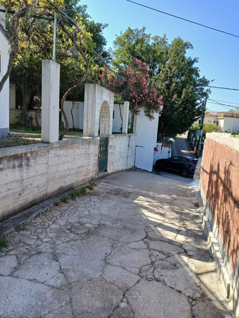 Prilazni put i betonska kapija na ulazu u dvorište sa zelenilom.