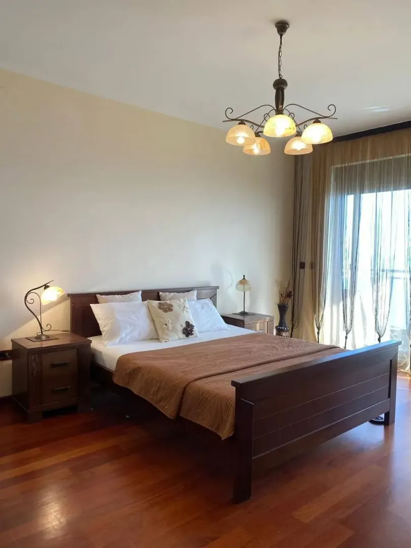 Namještena spavaća soba sa bračnim krevetom, noćnim stočićima i lusterom.