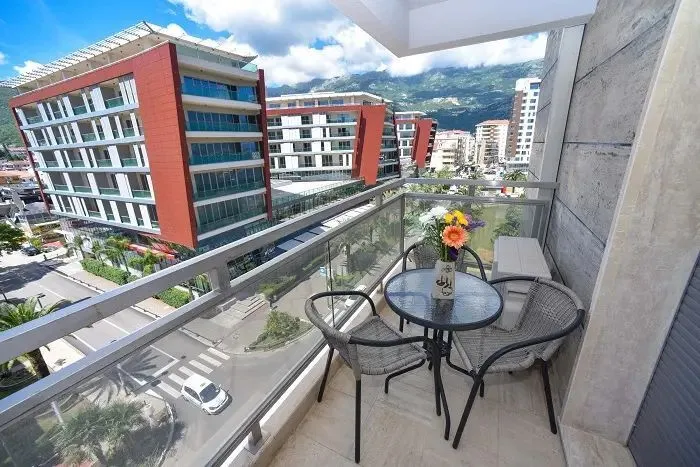 Furnished balcony with a table, chairs, and a view of surrounding buildings and mountains.